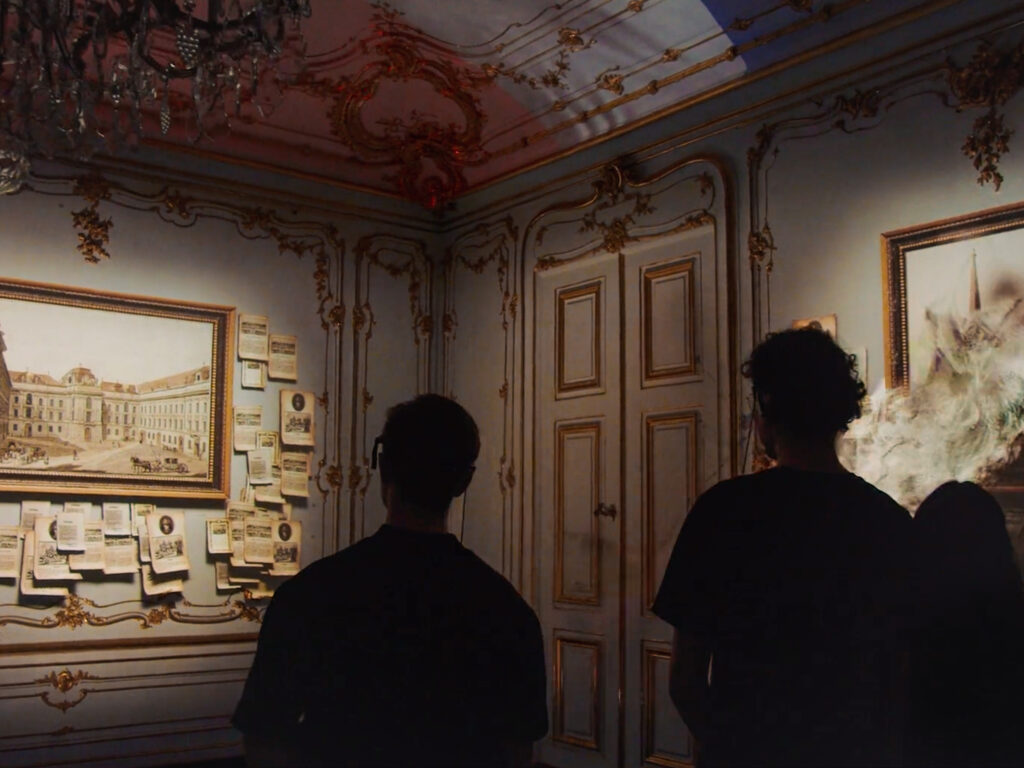 Drei Personen stehen mit dem Rücken zur Kamera, vor ihnen ein Projection Mapping aus Bilderrahmen, Briefen und historischen Figuren.